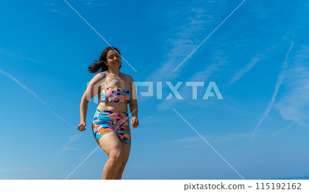 Woman in swimsuit walking on the beach. body positive, full, cellulite Woman in swimsuit walking on the beach. body positive, full, cellulite 115192162