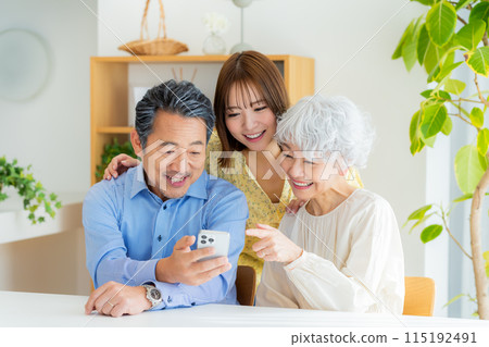 Senior couple and child looking at smartphone in the living room Senior couple and child looking at smartphone in the living room 115192491