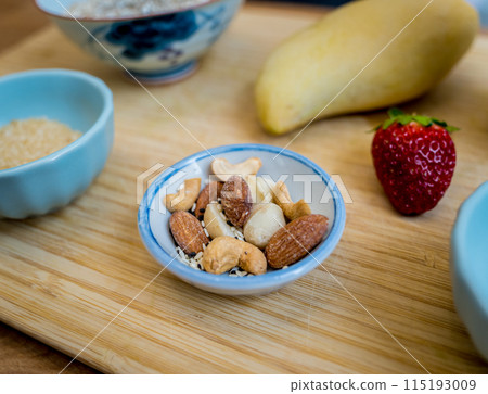Cutting board with ingredients for preparing bowl of oats with strawberries and mango 115193009