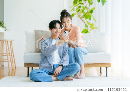 年輕夫婦在客廳放鬆，看著他們的智慧型手機 115193431