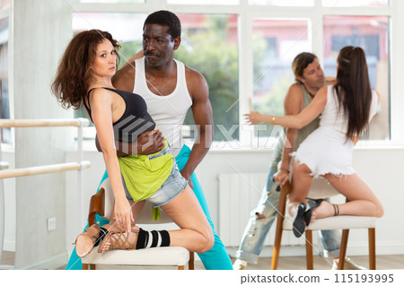 Woman in heels dances with man kneeling on chair 115193995