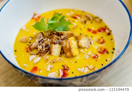 A bowl of pumpkin porridge with tofu and vegetables 115194479