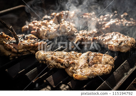High angle of appetizing and delicious meat pieces with smokes placed on barbecue grill in dark restaurant kitchen in daylight  115194792