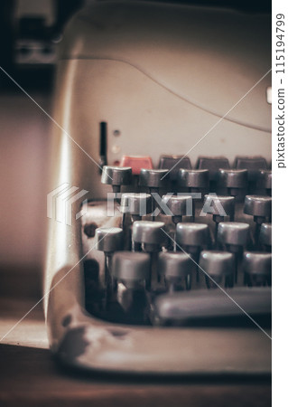 Closeup of vintage worn out typewriter and various keys with dust while placed on wooden table in daylight against dark blurred room Closeup of vintage worn out typewriter and various keys with dust while placed on wooden table in daylight against dark blurred room 115194799