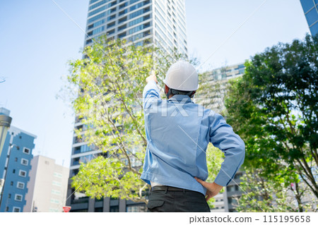 一個穿著工作服的男人抬頭看著辦公大樓 一個穿著工作服的男人抬頭看著辦公大樓 115195658