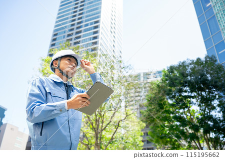 一個穿著工作服的男人抬頭看著辦公大樓 115195662