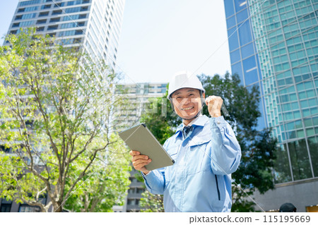 穿著工作服的男人抬頭看著辦公大樓，拳頭泵 115195669