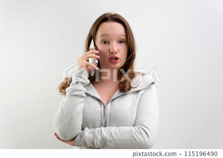 Cute high school girl with a very shocked expression talking on a cell phone Cute high school girl with a very shocked expression talking on a cell phone 115196490