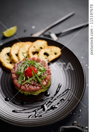 Tuna and avocado tartare on a dark ceramic plate Tuna and avocado tartare on a dark ceramic plate 115197678