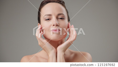 Beauty, health, cosmetics, anti-aging therapy and skin care concept - young beautiful brunette Caucasian woman touching her face skin with her hands, posing and looking at the camera as in a mirror Beauty, health, cosmetics, anti-aging therapy and skin care concept - young beautiful brunette Caucasian woman touching her face skin with her hands, posing and looking at the camera as in a mirror 115197692