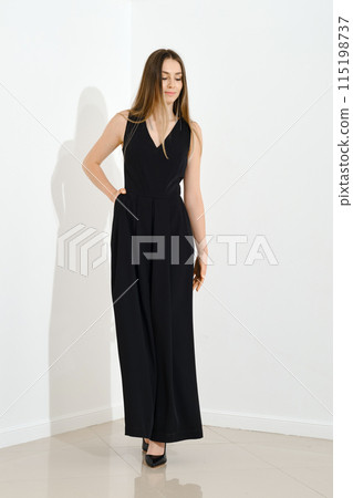 Cute smiling young woman in long sleeveless dress walking in bright room 115198737