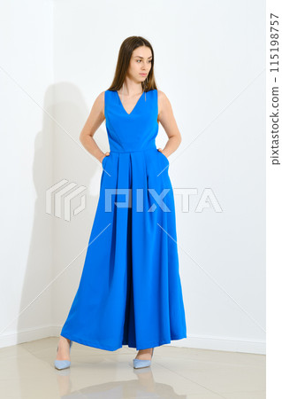 Stylish trendy woman in blue long sleeveless dress holding her hands in pockets 115198757