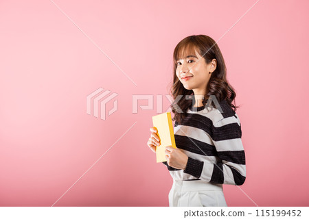 Portrait of beautiful Asian young woman teenage smiling holding a yellow book and reading, studio shot isolated on pink background with copy space Portrait of beautiful Asian young woman teenage smiling holding a yellow book and reading, studio shot isolated on pink background with copy space 115199452