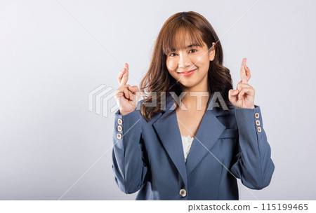 A beautiful young Thai woman is captured in a studio shot, her smiling face reflecting happiness and hope. With crossed fingers, she silently conveys her belief in good luck and positive vibes. A beautiful young Thai woman is captured in a studio shot, her smiling face reflecting happiness and hope. With crossed fingers, she silently conveys her belief in good luck and positive vibes. 115199465
