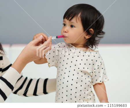 mother feeding liquid medicine to baby girl by syringe. sick toddler mother feeding liquid medicine to baby girl by syringe. sick toddler 115199683