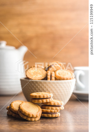 Chocolate Filled Cookies on a Wooden Table With a Cup and Pitcher in the Background 115199949