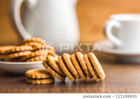 Chocolate Filled Cookies on a Wooden Table With a Cup and Pitcher in the Background Chocolate Filled Cookies on a Wooden Table With a Cup and Pitcher in the Background 115199950