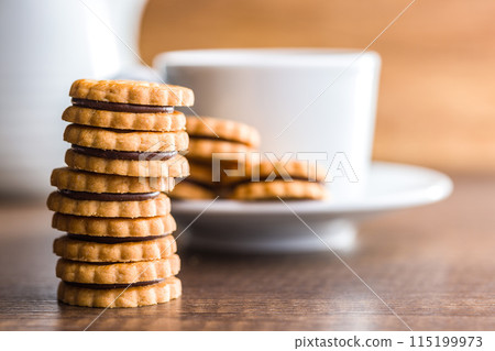 Chocolate Filled Cookies on a Wooden Table With a Cup and Pitcher in the Background 115199973