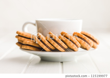 Chocolate Filled Cookies on a Saucer Beside a Cup 115199977