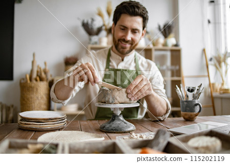 Smiling man working in a home pottery studio with laptop 115202119