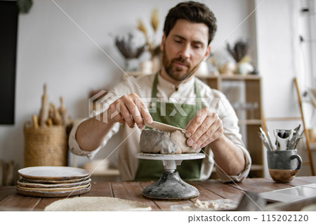 Smiling man working in a home pottery studio with laptop Smiling man working in a home pottery studio with laptop 115202120