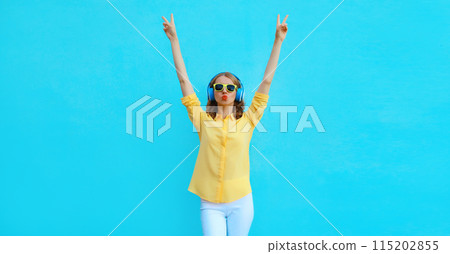 Happy modern young woman listening to music with headphones having fun on blue background Happy modern young woman listening to music with headphones having fun on blue background 115202855