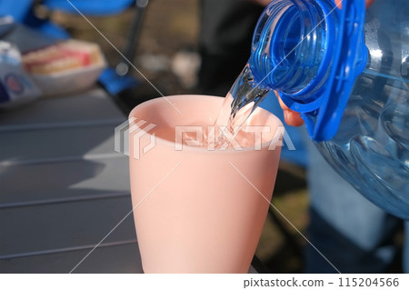Man pouring water from bottle to plastic cup on nature in sunny day. 115204566