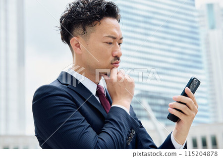 A businessman who looks at a smartphone and thinks 115204878