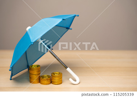 Coins stand under a blue umbrella. Financial risk insurance concept. Investments, deposits and loans. Risks and monetary transactions. Insurance contract and damage compensation Coins stand under a blue umbrella. Financial risk insurance concept. Investments, deposits and loans. Risks and monetary transactions. Insurance contract and damage compensation 115205339