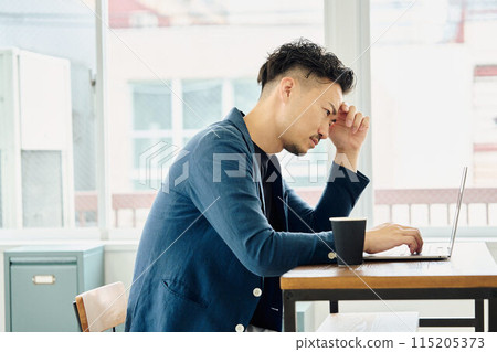 A man holding his head while looking at a computer 115205373