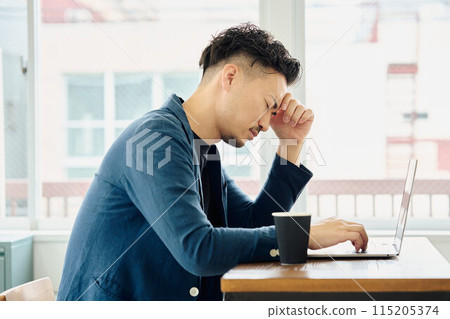 A man holding his head while looking at a computer 115205374