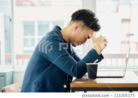 A man holding his head while looking at a computer A man holding his head while looking at a computer 115205375