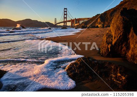 Bubbling seafoam on shore with sunset striking Golden Gate Bridge from sandy beach Bubbling seafoam on shore with sunset striking Golden Gate Bridge from sandy beach 115205398