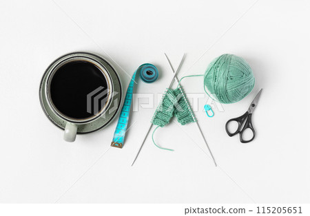 Composition of homemade needlework from cup of black coffee, scissors, mint ball for knitting and knitting needles, centimeter, pin. Hobbies of knitting warm clothes, toys, things for house. Composition of homemade needlework from cup of black coffee, scissors, mint ball for knitting and knitting needles, centimeter, pin. Hobbies of knitting warm clothes, toys, things for house. 115205651