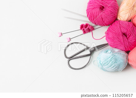 Composition of pink, blue, beige balls of knitting thread, knitting needles and scissors on gray background with place for text. Concept of home needlework, hobby for knitting warm clothes Composition of pink, blue, beige balls of knitting thread, knitting needles and scissors on gray background with place for text. Concept of home needlework, hobby for knitting warm clothes 115205657