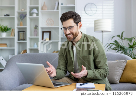 Smiling man talking during a video call on his laptop in a bright and modern home office space. Smiling man talking during a video call on his laptop in a bright and modern home office space. 115205973