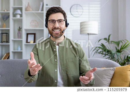 A smiling man with a headset having a video call while sitting in his home office. Remote work and virtual communication concept. A smiling man with a headset having a video call while sitting in his home office. Remote work and virtual communication concept. 115205979