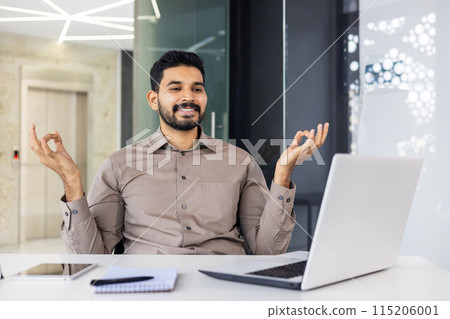 A man, dressed in a brown shirt, practices meditation and relaxation techniques at his workspace. He is seated with a laptop, notebook, and pen, demonstrating balance amidst a busy work environment. 115206001