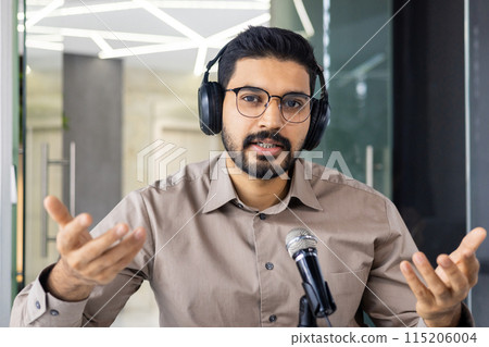 Man wearing headphones speaking into a microphone during a video call in a contemporary office environment. Man wearing headphones speaking into a microphone during a video call in a contemporary office environment. 115206004