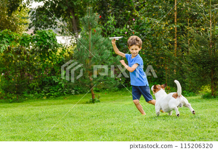 Kid playing with paper airplane and dog outdoors at backyard lawn 115206320