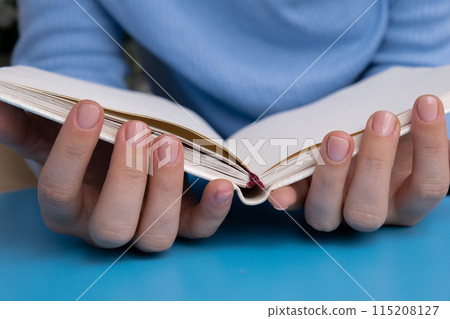 Pastel softness manicured nails with paper notebook on blue background. Woman showing her new manicure in colors of pastel palette. Simplicity decor fresh spring vibes earth-colored neutral tones  115208127