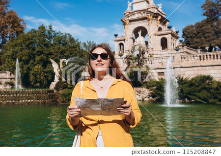 Young female tourist with paper map and phone visiting Ciutadella Park in Barcelona. Concept of travel, tourism and vacation in city, Traveling Europe Young female tourist with paper map and phone visiting Ciutadella Park in Barcelona. Concept of travel, tourism and vacation in city, Traveling Europe 115208847