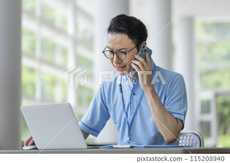 設施工作人員在筆記型電腦上工作時使用智慧型手機交談的圖片 115208940