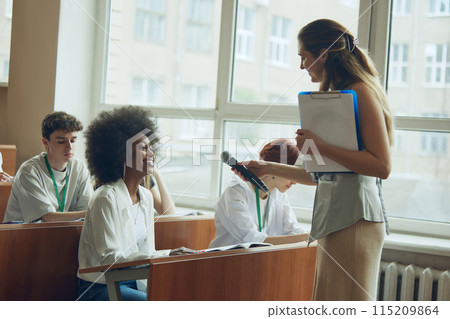 Lecturer interacting with students attending workshop. Well-lit university auditorium. Discussing students exchange 115209864