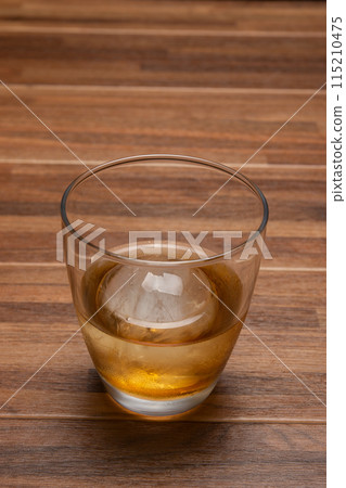 Whiskey on the rocks with round ice cubes on a wooden table 115210475
