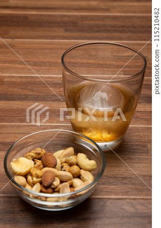Whiskey on the rocks with round ice cubes and snacks on a wooden table 115210482