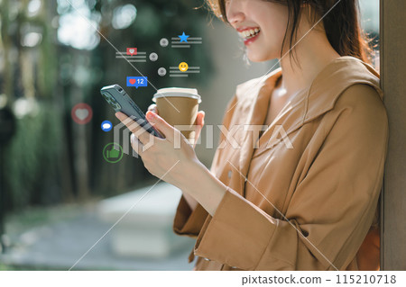 A cheerful young woman engaging with social media on her smartphone, receiving likes and reactions while holding a coffee cup outdoors. 115210718