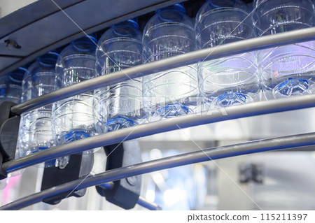 The empty drinking water bottles hanging on the conveyor belt for filling process. The empty drinking water bottles hanging on the conveyor belt for filling process. 115211397