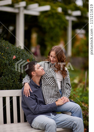 Autumn Romance: Young Couple Embracing and Kissing on Park Bench. Young couple kissing and rejoices at the lake. lovely young couple kissing outdoors in autumn. Embraced in Autumn's Warmth: Couple's 115211619