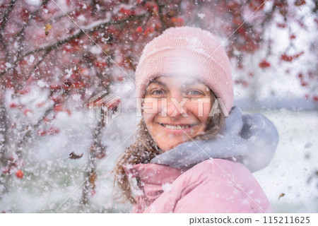 Winter Elegance: Portrait of a Beautiful Girl in a Snowy European Village. Winter lifestyle portrait of cheerful pretty girl. Smiling and having fun in the snow park. Snowflakes falling down 115211625